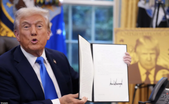 Trump holds a signed executive order during an Oval Office appearance.