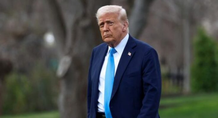 former President Donald Trump in navy suit and blue tie standing outdoors near trees