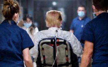 medical team escorts patient in wheelchair down hospital corridor
