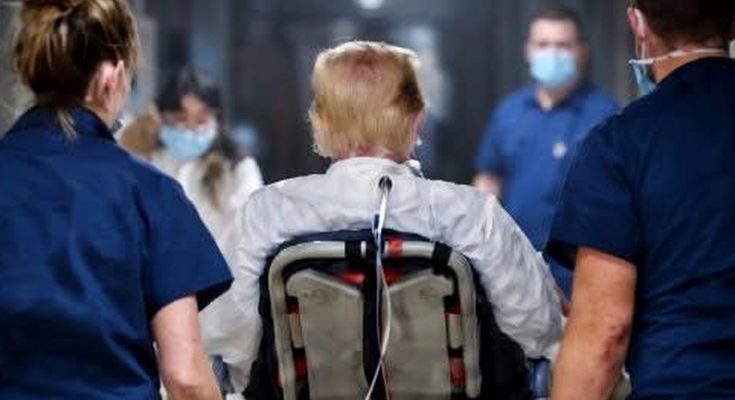 medical team escorts patient in wheelchair down hospital corridor