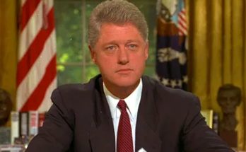 president Bill Clinton seated at Oval Office desk with American flag and busts in