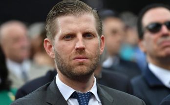 man in suit at formal event, serious expression, blurred crowd