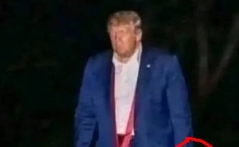former President Donald Trump walks outdoors at night in a blue suit and red tie