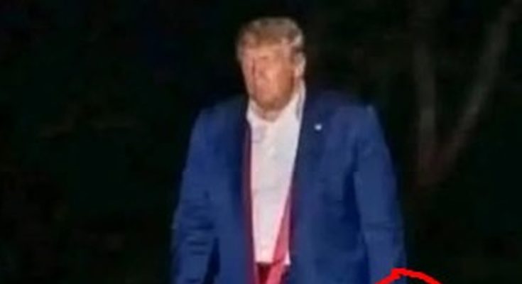 former President Donald Trump walks outdoors at night in a blue suit and red tie