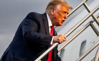 donald Trump descending airplane stairs in dark suit and red tie