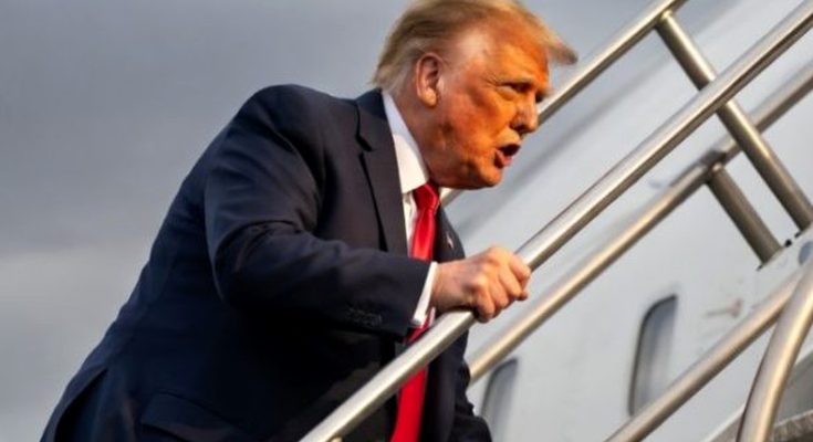 donald Trump descending airplane stairs in dark suit and red tie