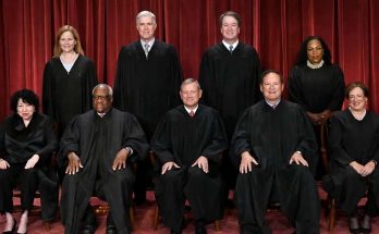 supreme Court justices in formal robes against red curtain backdrop
