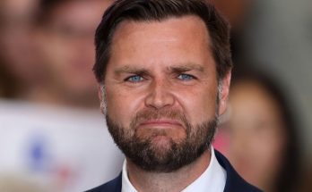 senator JD Vance with blue eyes and beard wearing navy suit at public event