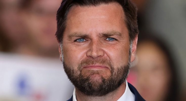 senator JD Vance with blue eyes and beard wearing navy suit at public event