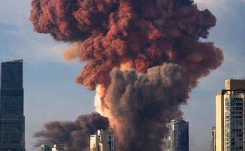 massive reddish-brown and black smoke plume rising above city skyline with modern