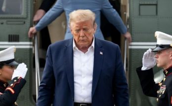 former President Donald Trump descends steps from a military transport plane as two