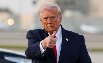 former President Donald Trump giving a thumbs-up gesture outdoors in a suit