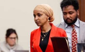 woman in red blazer and beige headscarf holding folder in courtroom