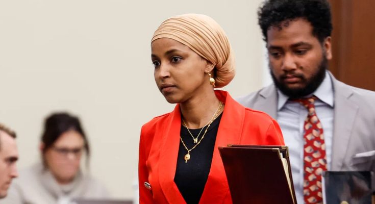 woman in red blazer and beige headscarf holding folder in courtroom
