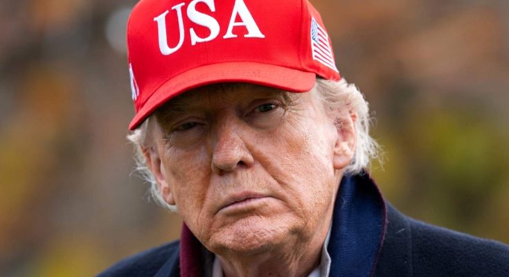 donald Trump wearing a red USA baseball cap with American flag patch, outdoors with