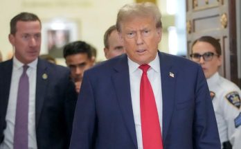 former President Donald Trump walks through a hallway wearing a blue suit and red tie