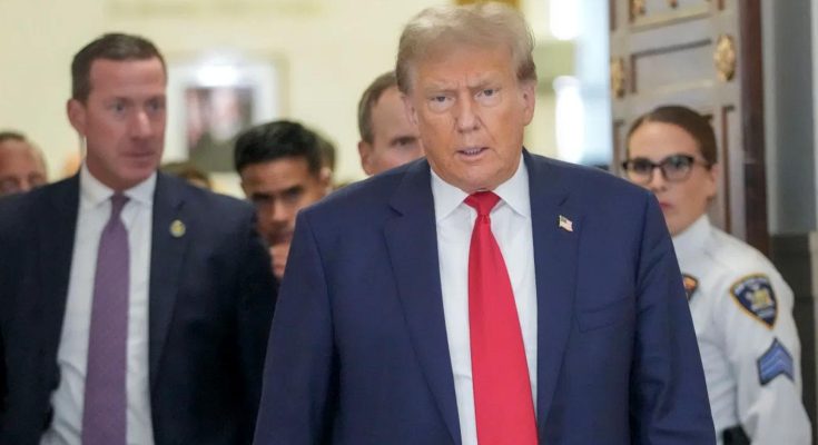 former President Donald Trump walks through a hallway wearing a blue suit and red tie