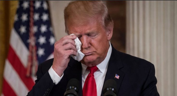 former President Donald Trump wiping his eye with a tissue at a podium with an American