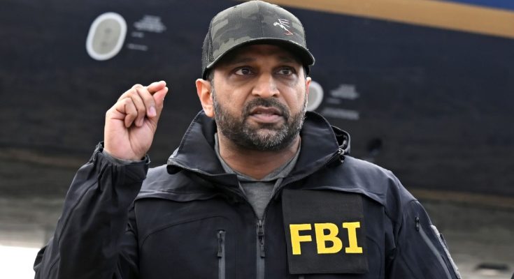 FBI agent in black jacket and cap gestures while standing in front of aircraft