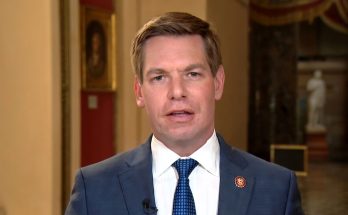 man in suit and tie with U.S. House pin speaking indoors in formal setting