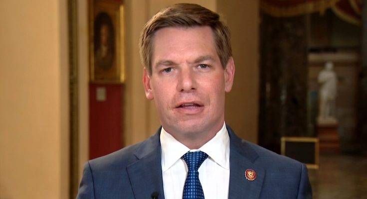man in suit and tie with U.S. House pin speaking indoors in formal setting