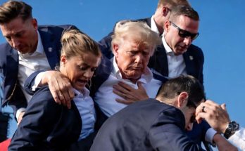 donald Trump being supported by aides outdoors under clear blue sky