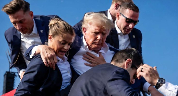 donald Trump being supported by aides outdoors under clear blue sky