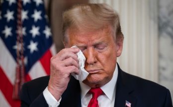 donald Trump wiping his eye with a tissue in front of an American flag