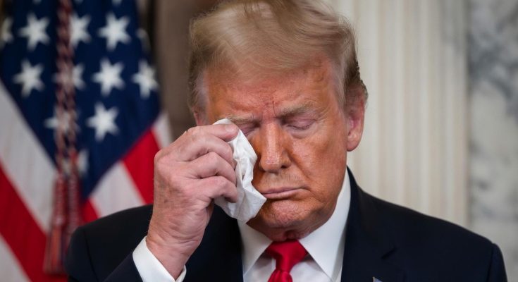 donald Trump wiping his eye with a tissue in front of an American flag