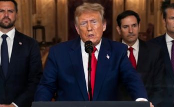 former President Donald Trump speaking at podium with three men in suits standing behind