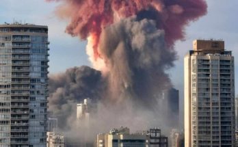 massive explosion sends fiery smoke plume skyward between towering city skyscrapers