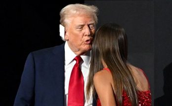 man in suit with red tie speaking to woman in red dress on stage