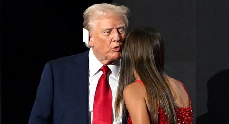 man in suit with red tie speaking to woman in red dress on stage