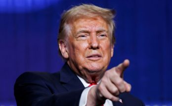 donald Trump pointing finger at camera during speech with blue backdrop