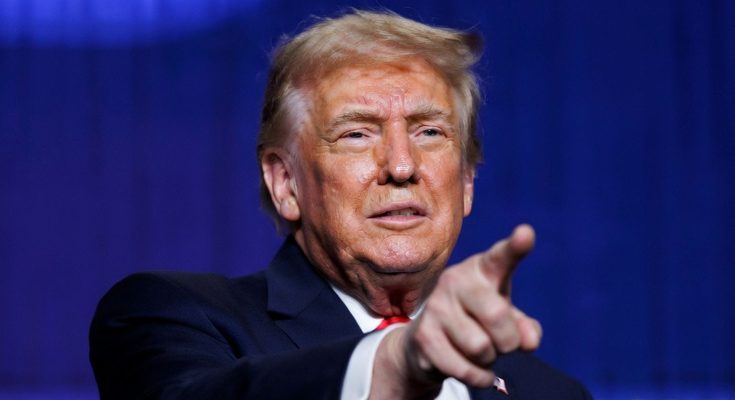 donald Trump pointing finger at camera during speech with blue backdrop