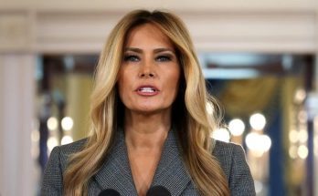 melania Trump speaking at a press conference in the White House with American flag visible